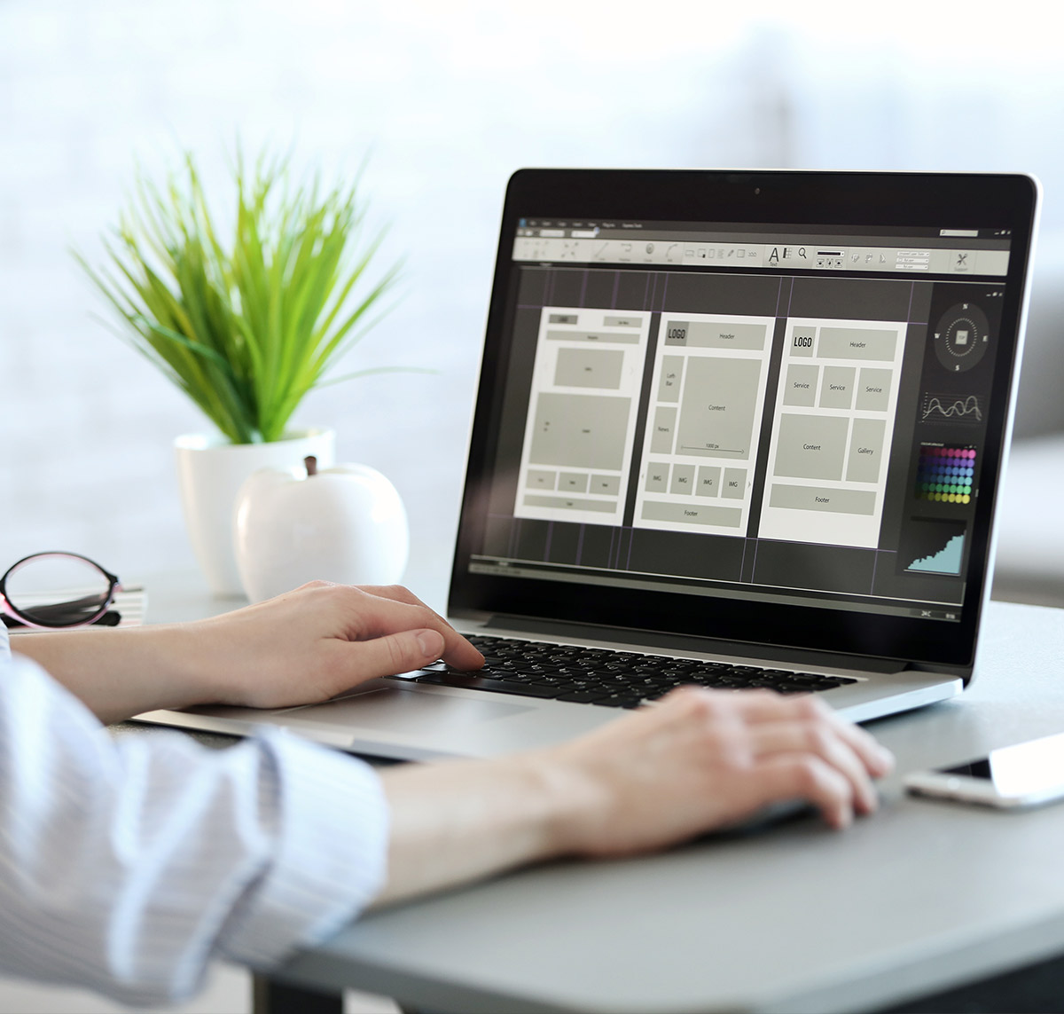 Eine Person arbeitet an einem Laptop, der ein Layout-Design für eine Website zeigt, umgeben von Pflanzen und Büromaterial.