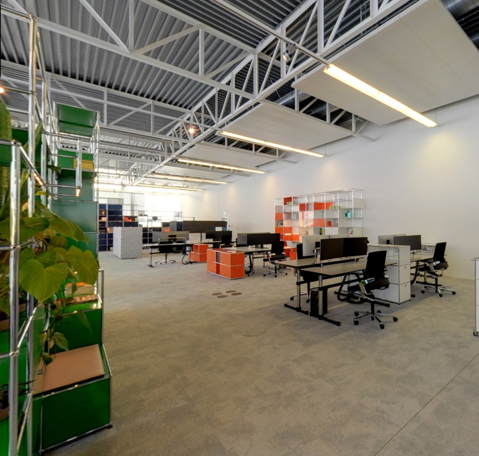 Modernes Büro mit mehreren Arbeitsplätzen, Computern und Pflanzen, ideal für kreative Zusammenarbeit und Produktivität.