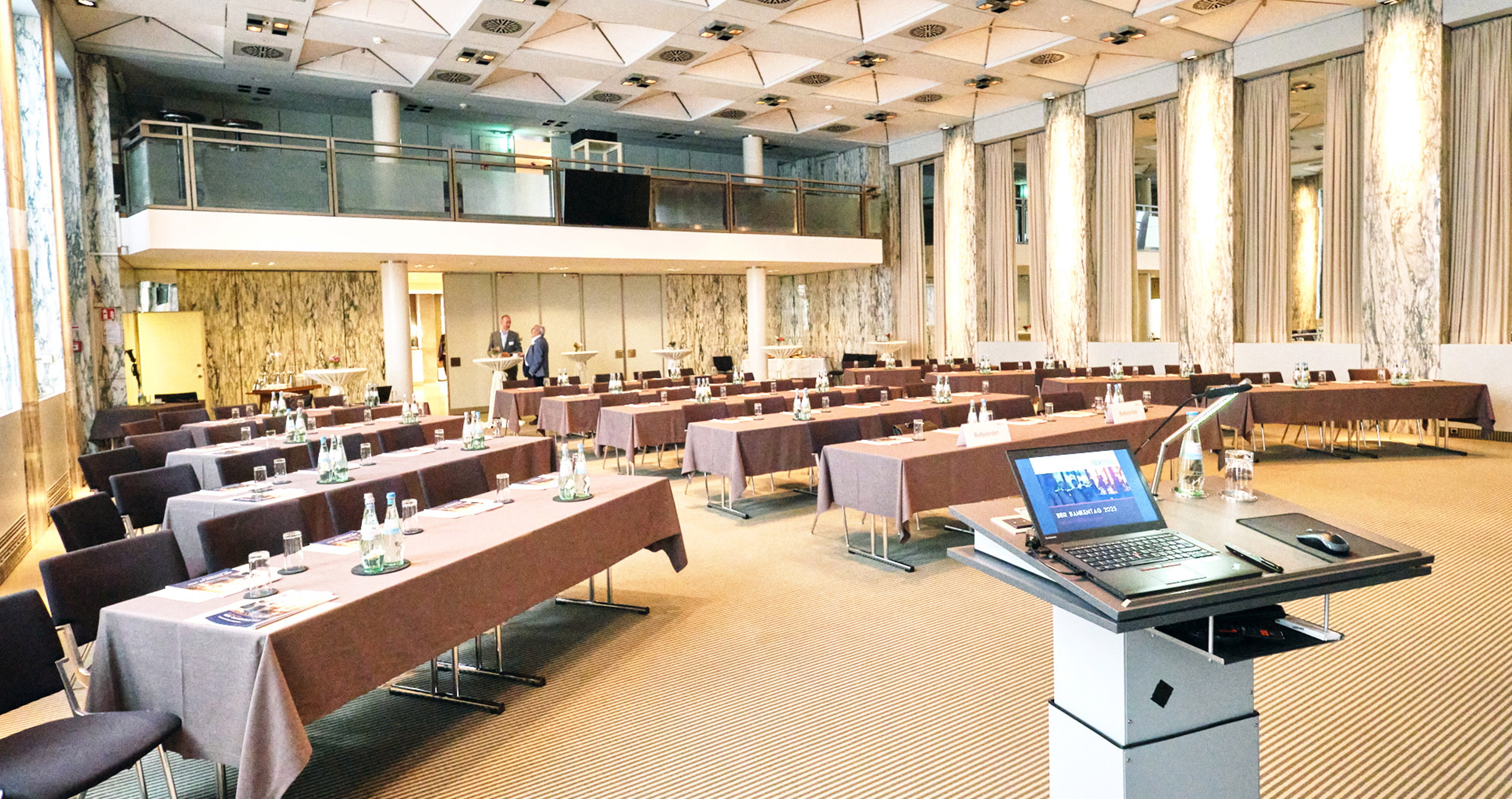 Moderner Konferenzraum mit Tischen, Stühlen und technischer Ausstattung für Veranstaltungen und Meetings.