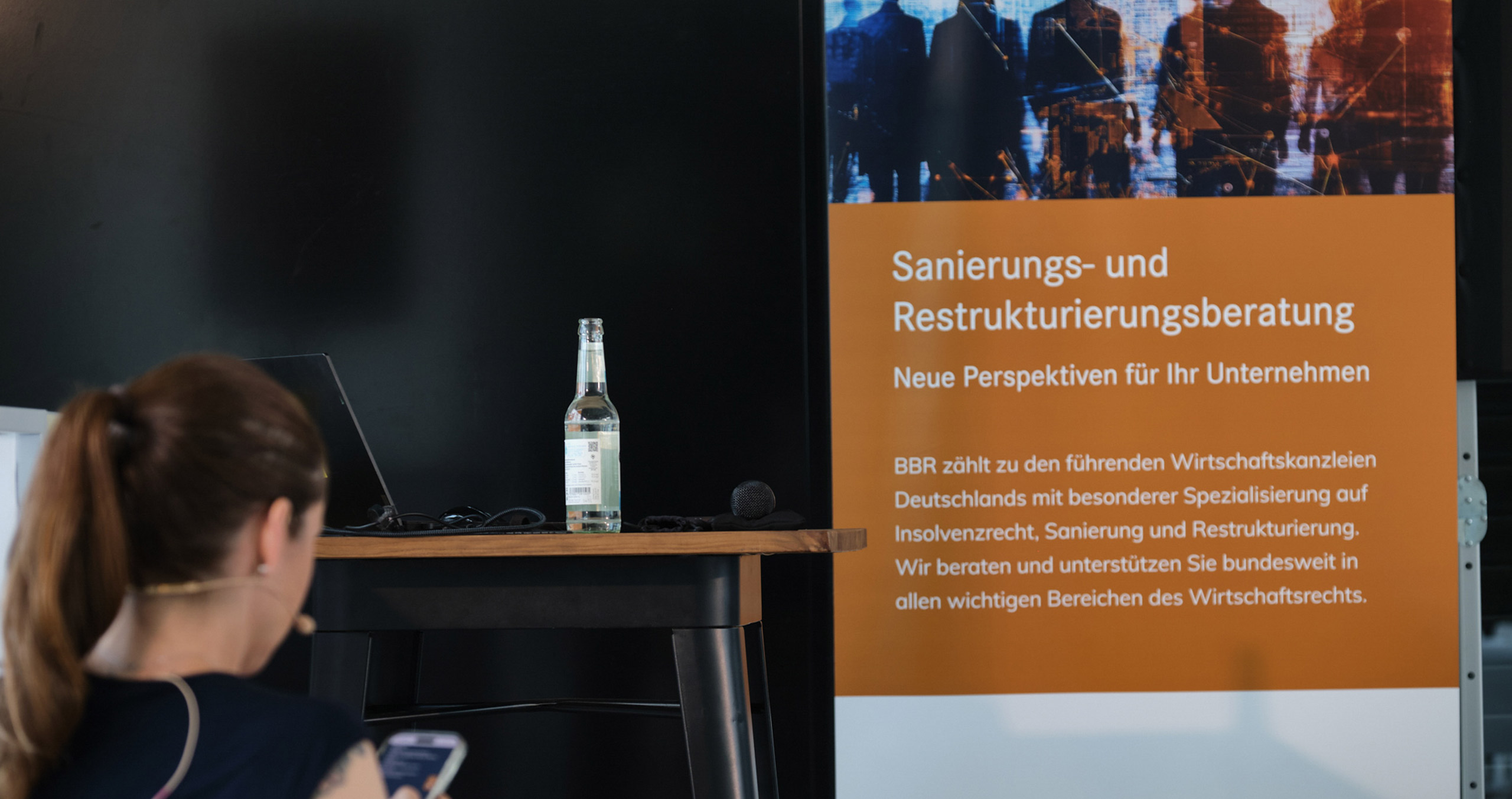 Eine Präsentation über Sanierungs- und Restrukturierungsberatung mit einem Tisch, einer Flasche Wasser und einer Person im Vordergrund.