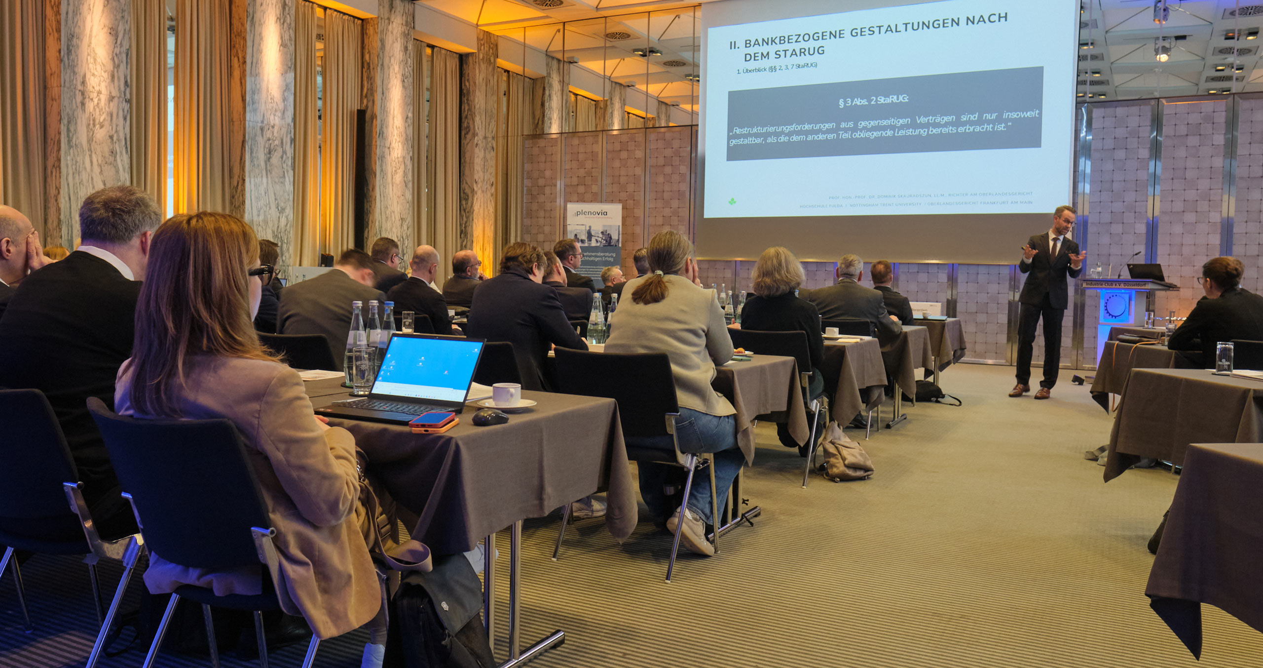 Konferenzteilnehmer hören einem Vortrag über bankbezogene Gestaltungen nach dem StarUG in einem modernen Tagungsraum.