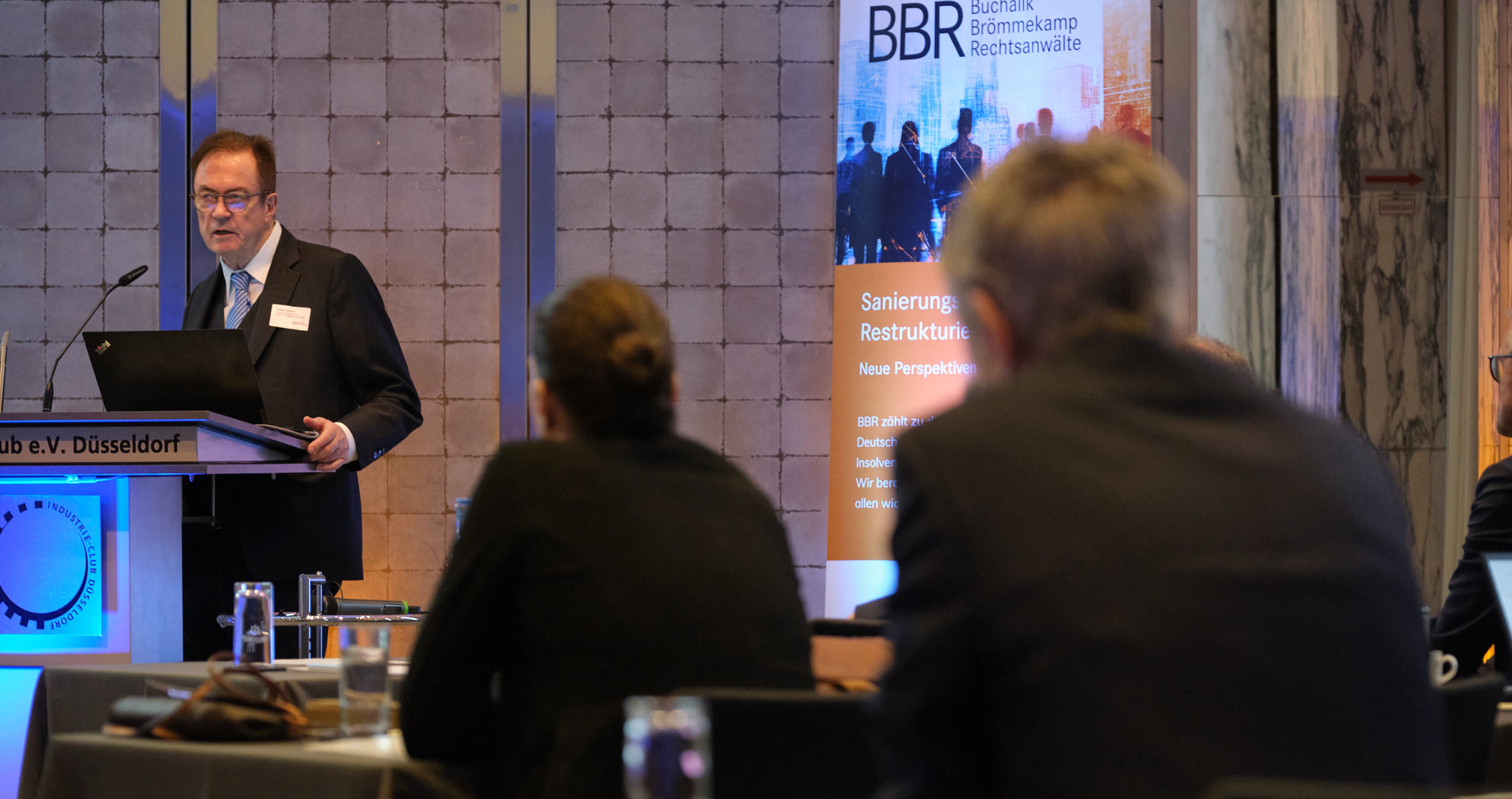 Ein Redner präsentiert auf einer Konferenz über Unternehmenssanierung und Rechtsberatung in Düsseldorf.