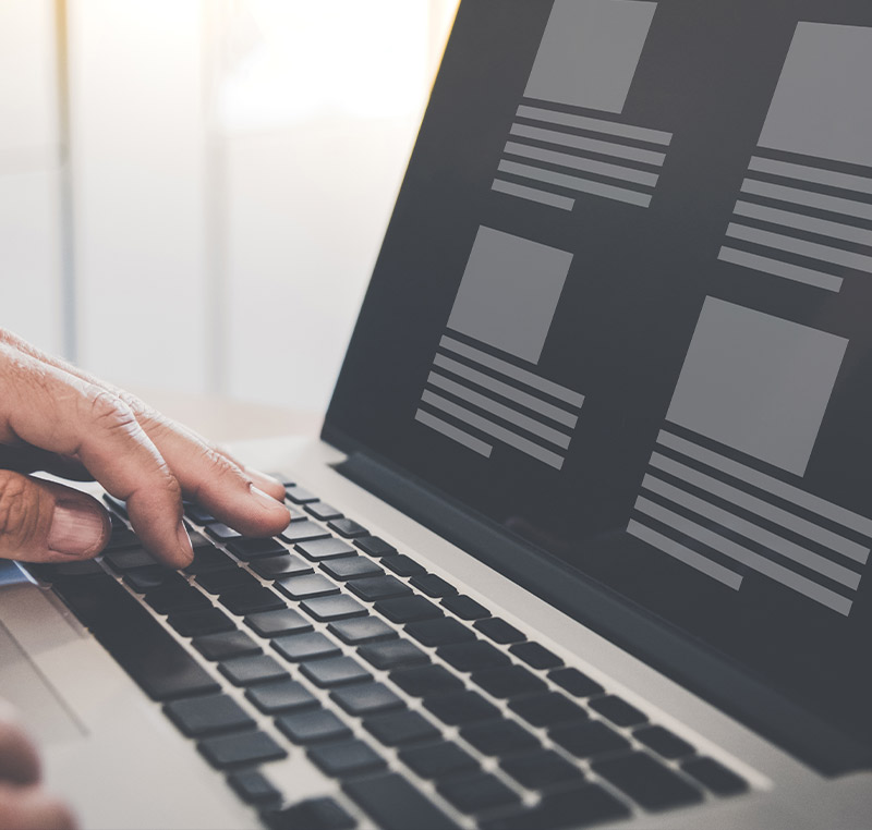 Eine Person tippt auf einer Laptop-Tastatur, während auf dem Bildschirm ein abstraktes Layout mit Platzhaltern für Text und Bilder zu sehen ist.