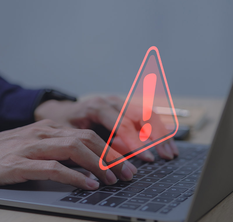 Nahaufnahme von Händen, die auf einer Laptop-Tastatur tippen, mit einem darübergelegten, leuchtend roten Warnsymbol in Form eines Ausrufezeichens.