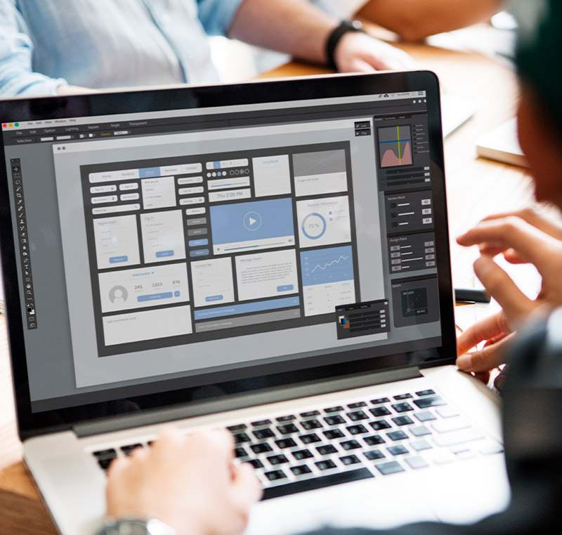 Ein Designer arbeitet an einem Laptop an einem komplexen Benutzeroberflächen-Layout mit verschiedenen grafischen Elementen und Diagrammen.
